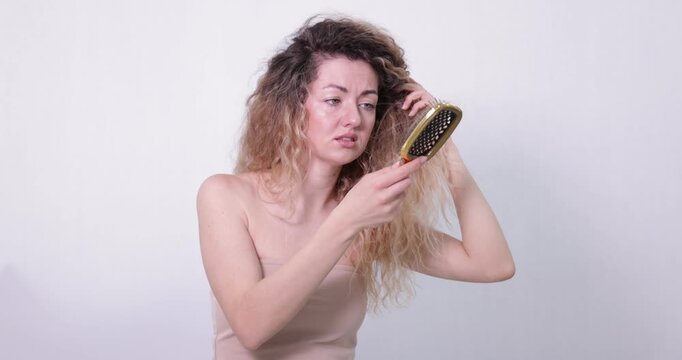 Unhappy woman trying to brush her tangled hair on light grey background