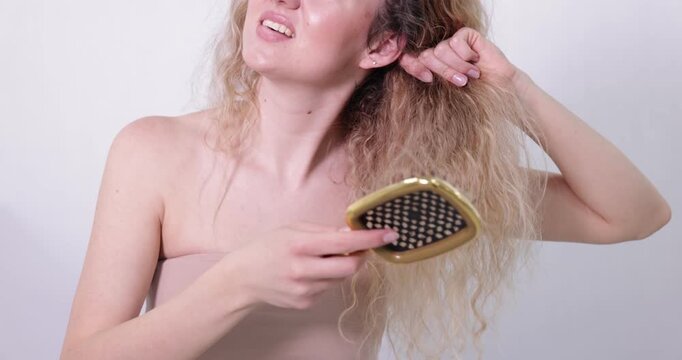 Woman trying to brush her tangled hair on light grey background, closeup