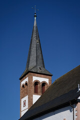 Fototapeta premium Close-up of the historic church tower in Gemünd, Germany. Features a slate roof, sandstone details, and a clear blue sky background.