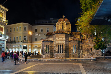 Obraz premium The illuminated 11th century Church of Panagia Kapnikarea, one of the oldest churches in Athens surrounded by the lively Ermou Street shopping district in Athens, Greece at night.