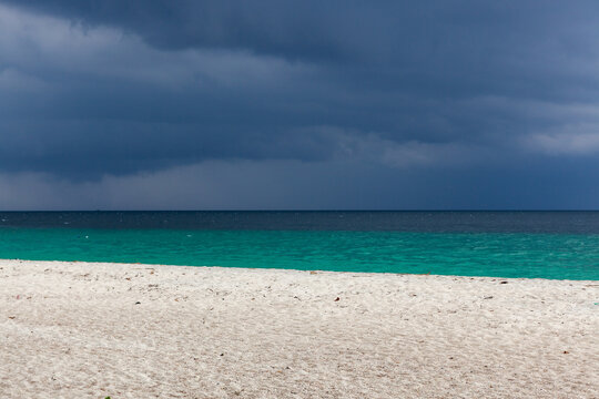 Tropical beach in Koh Adang, Thailand, with clear turquoise water and stormy weather. White sand shoreline under dramatic skies with blue horizon.