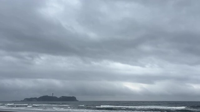 曇り空の下に広がる荒れた海と灯台のある島