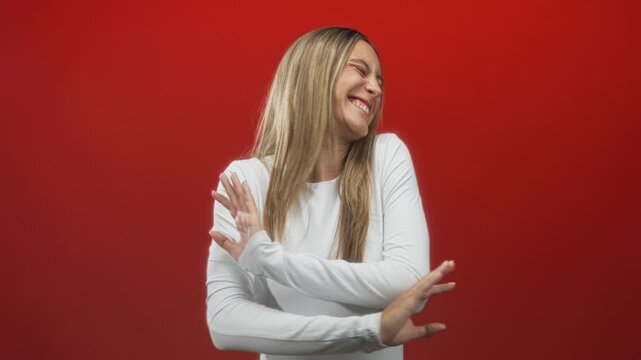 Woman laughing with hands waving and blurred gesture, smiling face and long hair against red studio backdrop; joy.