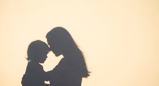 Shadow of mother and child embracing tenderly against a warm, textured wall