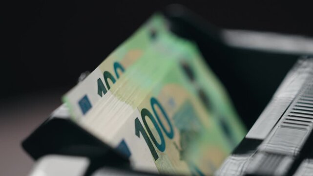 Close-up view of &euro;100 bills in electronic money counter. Banking and cash flow concept.
