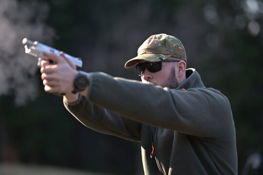 Man practicing handgun shooting outdoors in tactical gear and camouflage cap during target training session