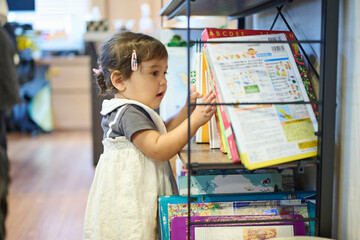 本棚の絵本を手に取る幼児 © One