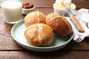Fototapeta premium Tasty hot cross buns, butter, raisins and milk on wooden table, closeup