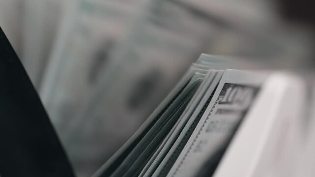 Close-up of cash counting machine with stacks of $100 bills. Finance concept.
