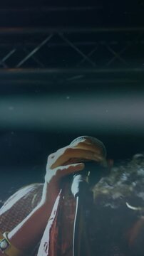 Vertical video: Woman singer starting song gripping mic tilting and tossing hair amid stage flares