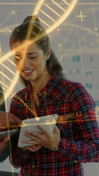Woman tapping tablet screen, reviewing bio data with peer, animated DNA helix sweeping over her