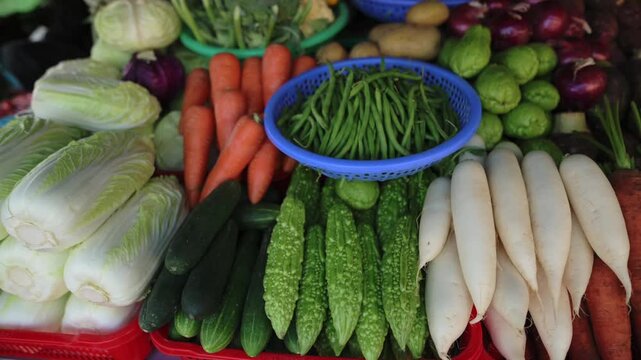 Fresh Vietnam Street Market Vegetables Arranged In Colorful Rows With Napa Cabbage, Carrots, White Radish, Bitter Gourd, Cucumbers And Blue Basket Of Green Beans, Vibrant Display Evokes Bustling