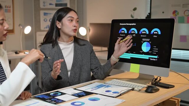 Businesswomen discussing consumer demographics on computer screen