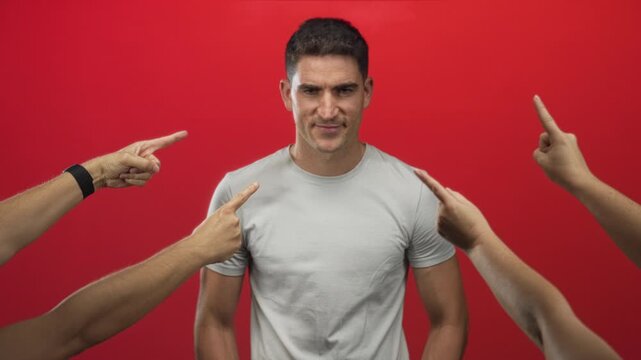 Man with multiple pointing fingers and a grimace in red studio wearing a gray tshirt; shame social judgment.