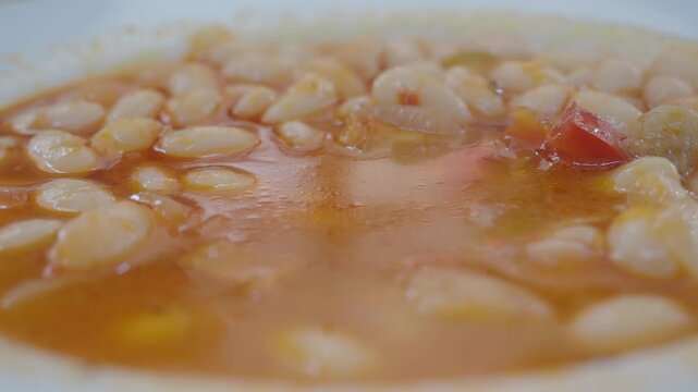 spoon pick white bean soup with vegetables in a pot