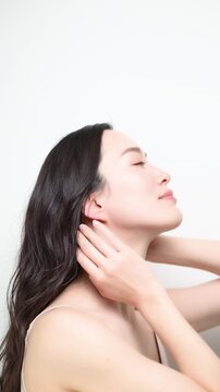 白背景に綺麗な黒髪かき上げるロングヘアでパーマの女性　ヘアケアやトリートメントイメージの縦動画の横顔　スローモーション