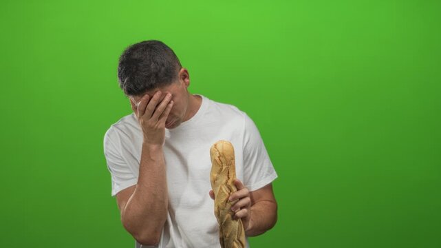 Young hispanic man holding a baguette and facepalm gesture in studio against a vivid green wall; frustration.