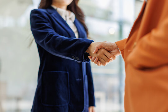 Two professional women exchange a handshake in a contemporary office setting, showcasing trust, collaboration, and the spirit of partnership in their meeting.