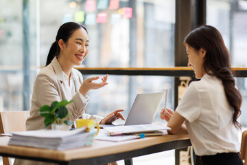 Obraz premium Happy Businesswomen Reviewing Documents Together in Modern Office Meeting