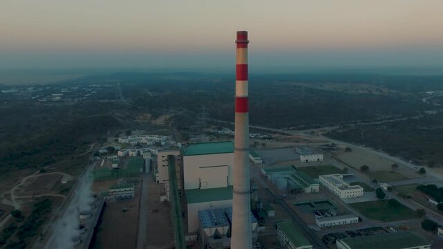 Thar Coal Power Plant in Pakistan at sunset, focusing on tall, red and white striped chimney and air vents. Left panning aerial orbit panning left.