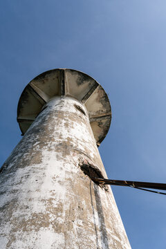 Low angle looking up at an weathered white concrete lighthouse against a clear blue sky at Koh Lanta Thailand