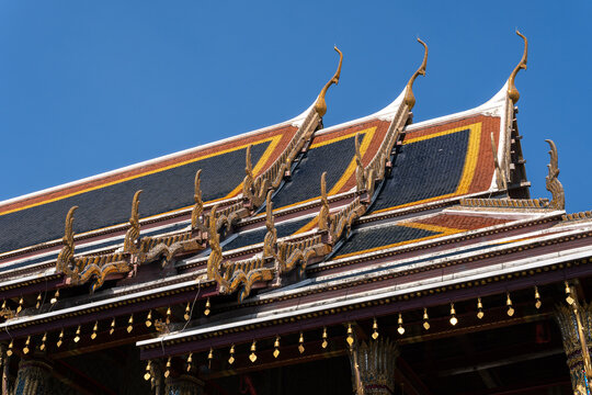 Traditional Thai temple roof with colorful tiered tiles and chofah ornaments against blue sky