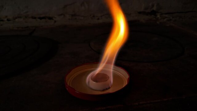 Hexamine solid fuel tablet burning with bright orange flame in the dark. 