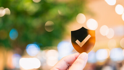 Hand holding a shield symbol with check mark against blurred bokeh background. Business concept of...