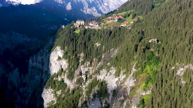 Aerial view of M&uuml;rren village perched on cliff edge overlooking deep valley with snow capped Swiss Alps peaks in background