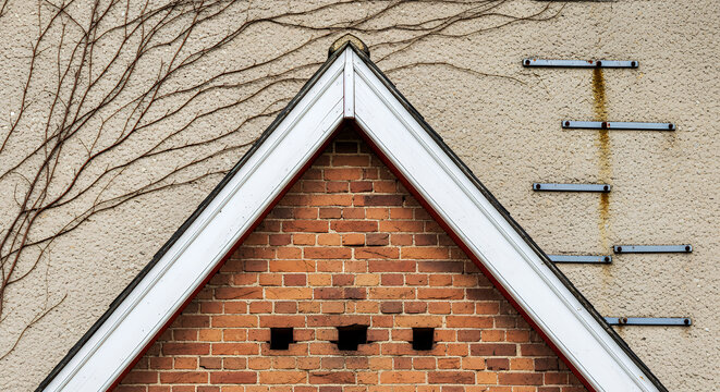 Triangular brick gable with white trim and exposed brackets on beige wall triangular roof