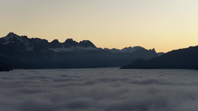 Dark alpine mountain silhouettes above dense cloud inversion during early dawn near Walensee, Switzerland