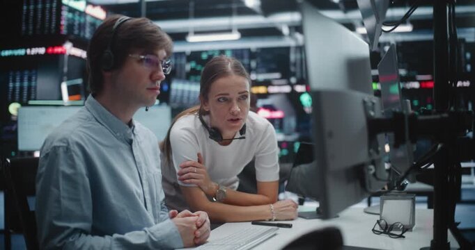 Female Manager Advising Young Male Trader in Busy Financial Office. Analyst With Supervisor Review Complex Analytics on Display, Gesturing Towards Key Data Points. Mentorship and Office Coordination.