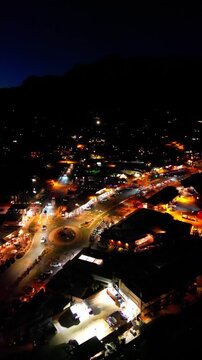 Vertical drone shot showcasing the bright city lights of a Sedona roundabout at night with dark mountains visible in the distance.