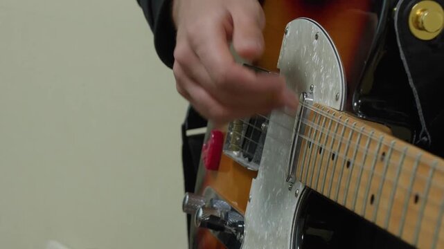 A close-up, static shot of a musician's hand strumming the strings of a sunburst Telecaster-style electric guitar. The focus is on the rhythmic playing technique and musical performance.