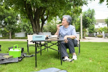 Fototapeta premium Senior woman enjoying food during camping in a park