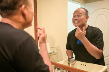 Fototapeta premium Asian senior man brushing teeth in front of a bathroom mirror