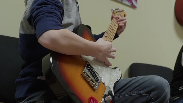 Close-up video of a young person playing a sunburst electric guitar. Their hands move across the fretboard and strings, demonstrating practice and skill. Focus is on the instrument and technique.