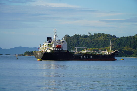 A large Pertamina industrial tanker floats quietly in calm waters near a green, forested island. Indonesia - Sibolga, March 15, 2026