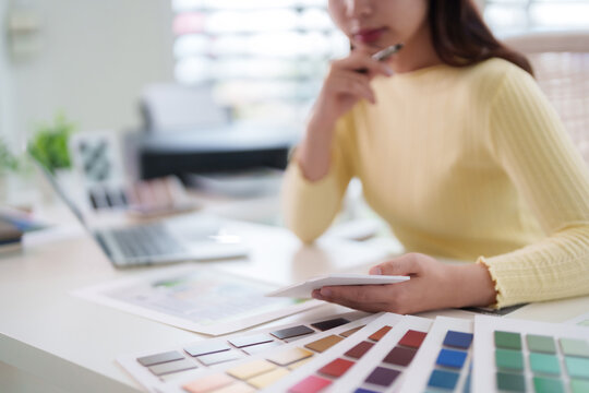 Asian adult woman creative designer selecting color palette swatches planning project design at home office studio workspace