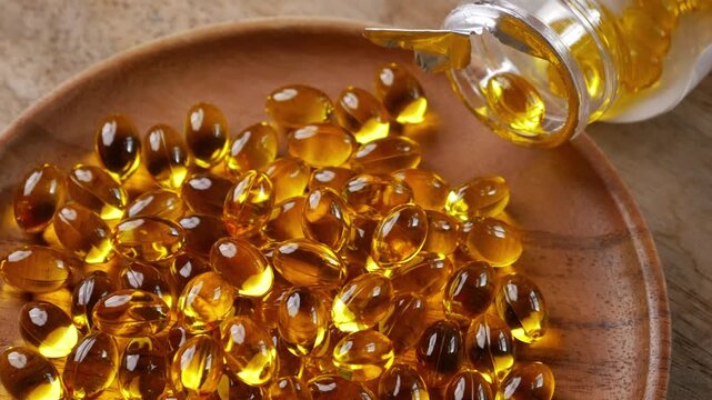 Golden yellow fish oil omega-3 supplement softgel capsules piled on wooden plate, health nutrition vitamin dietary supplement concept