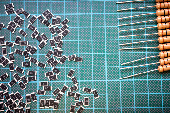 Surface mount resistors and through hole resistors on cutting mat, electronic components comparison background