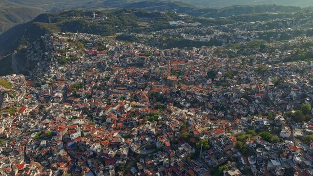 Flyover in orbit establishing shot of the town of Taxco on a sunny day, colonial architecture and tile roofs, state of Guerrero, Mexico