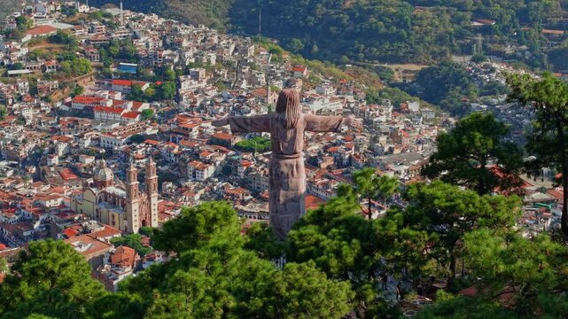 Telefoto aerial view of the Monumental Christ of Taxco with the town of Taxco in the background, featuring the Santa Prisca temple and colonial architecture with tile roofs, sunny day, Mexico