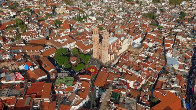 Aerial view of Taxco de Alarcon with the Temple of Santa Prisca and the Christmas flower or poinsettia, a city with colonial architecture and tiled roofs, on a sunny day.