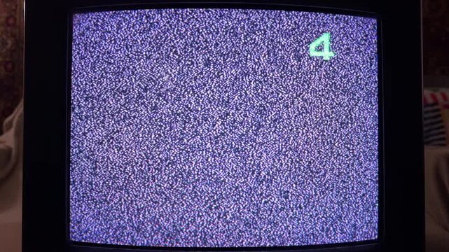 A vintage television screen flickers with purple-tinted static noise and a green number four. This grainy, cold display evokes a lonely or eerie feeling in the dark room.
