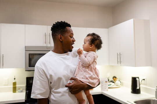 Father holding baby daughter smiling and bonding at home, multiracial family