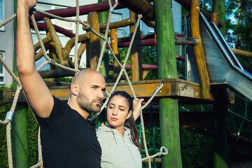 Obraz premium Young Fitness Couple Posing Together at a Wooden Outdoor Workout Station Looking Away