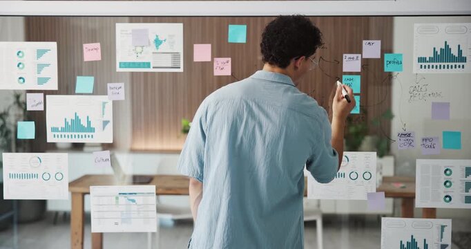 Man, glass wall and writing with notes at office for planning, charts and back at marketing company. Person, board and review with graphs, stats and problem solving with statistics at media agency
