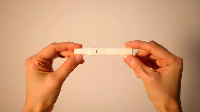 Two hands holding a small white object against a plain background. The object appears to be a test strip or similar item, emphasizing a medical or diagnostic theme.