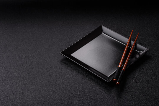 An empty ceramic square black plate with chopsticks for Asian food. An empty square plate